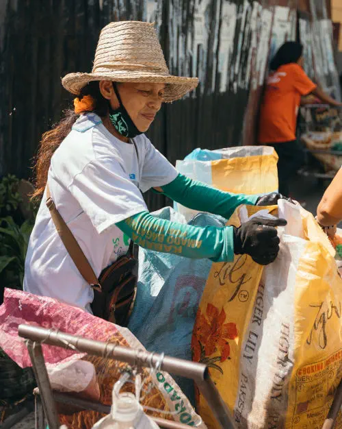woman in straw hat with glove on packing plastic into bags